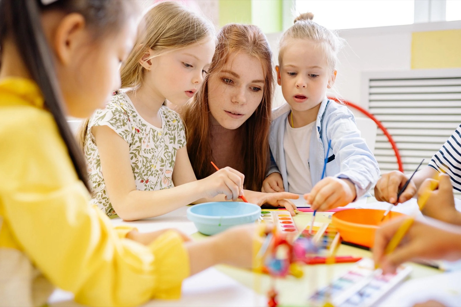 A teacher painting with a small group of young children at a classroom table
